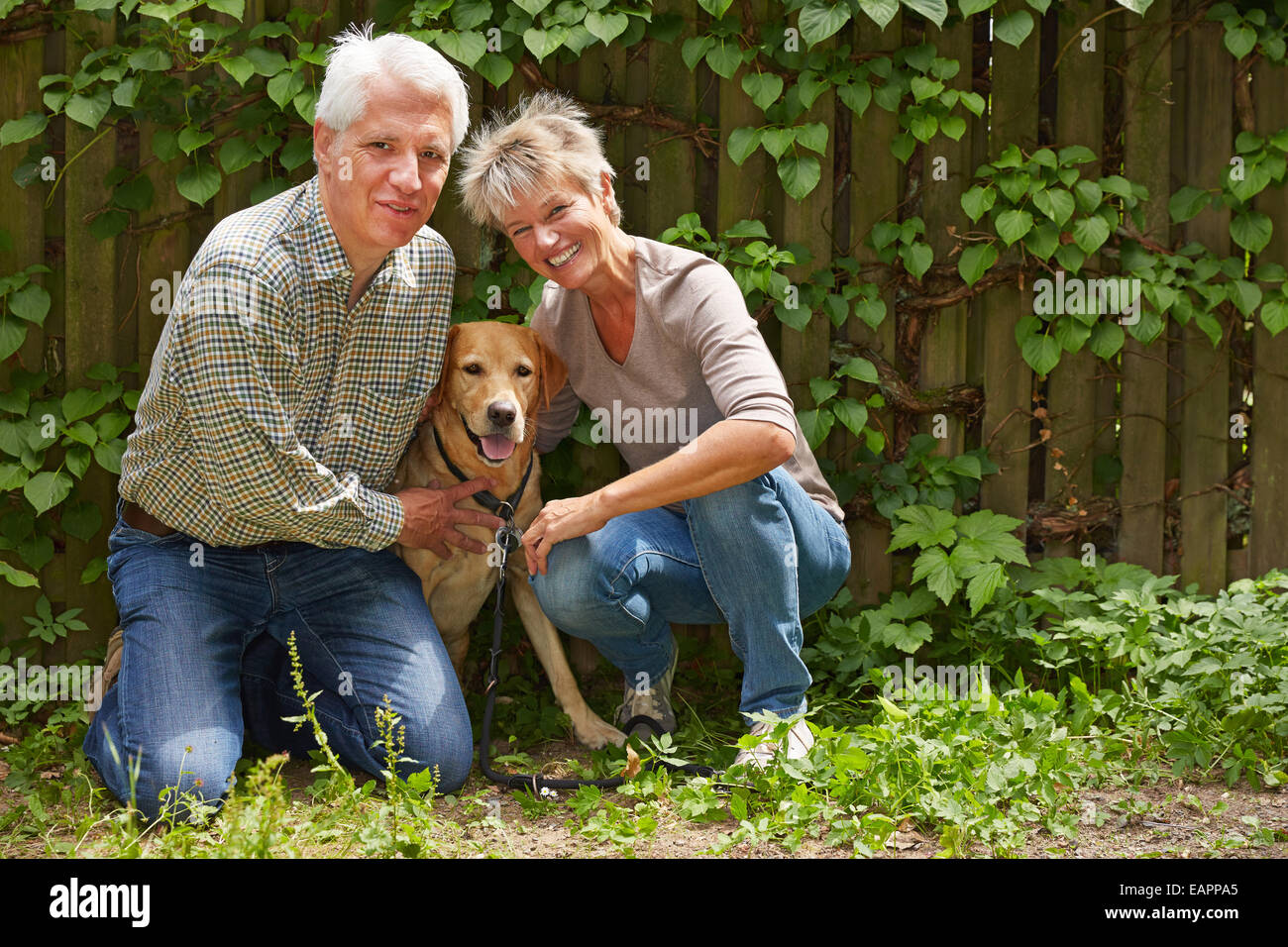 Un homme âgé et smiling woman sitting avec leur chien dans un jardin Banque D'Images