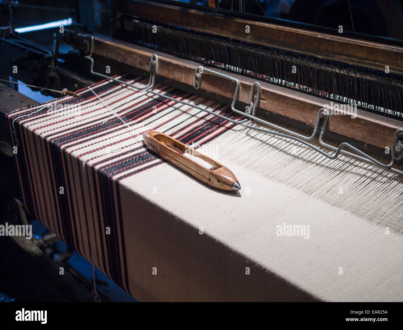 Volant sur un tissu à rayures. Un volant avec la laine blanche repose sur un morceau de tissu à rayures étant tissés sur une usine vintage Banque D'Images