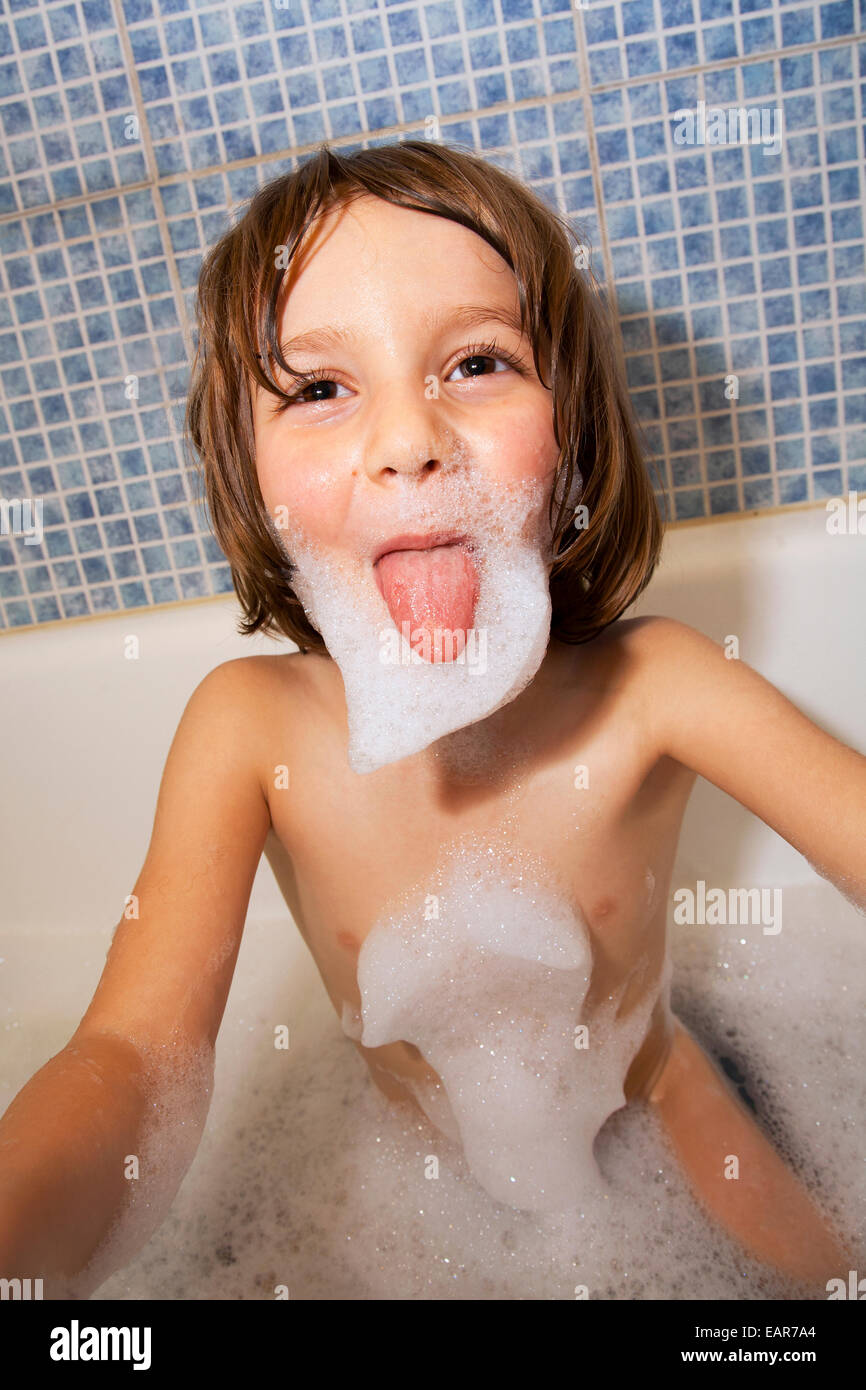 Six ans dans un bain de mousse poussant sa langue dehors. Banque D'Images