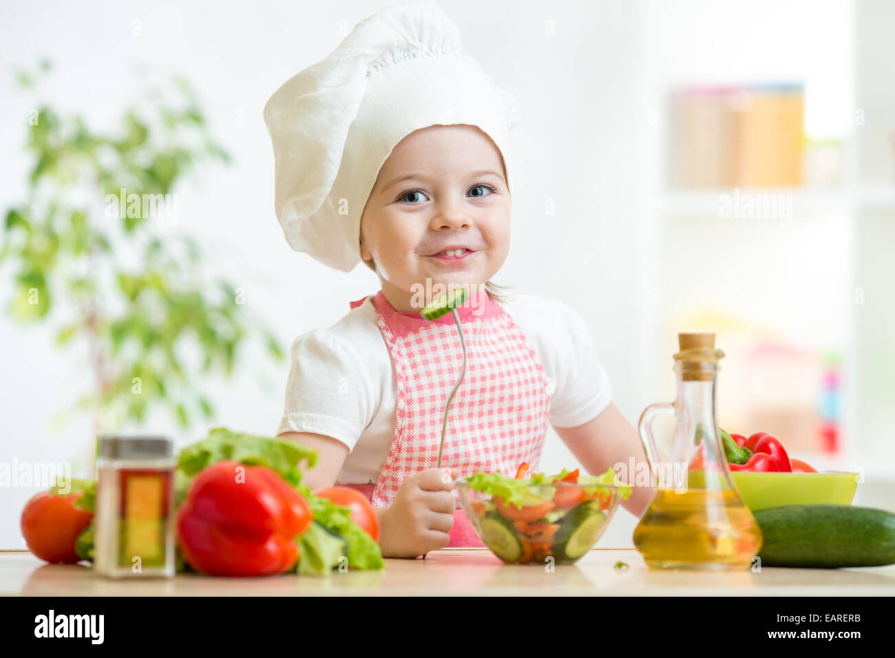 Fille enfant dans cook hat manger des légumes Banque D'Images