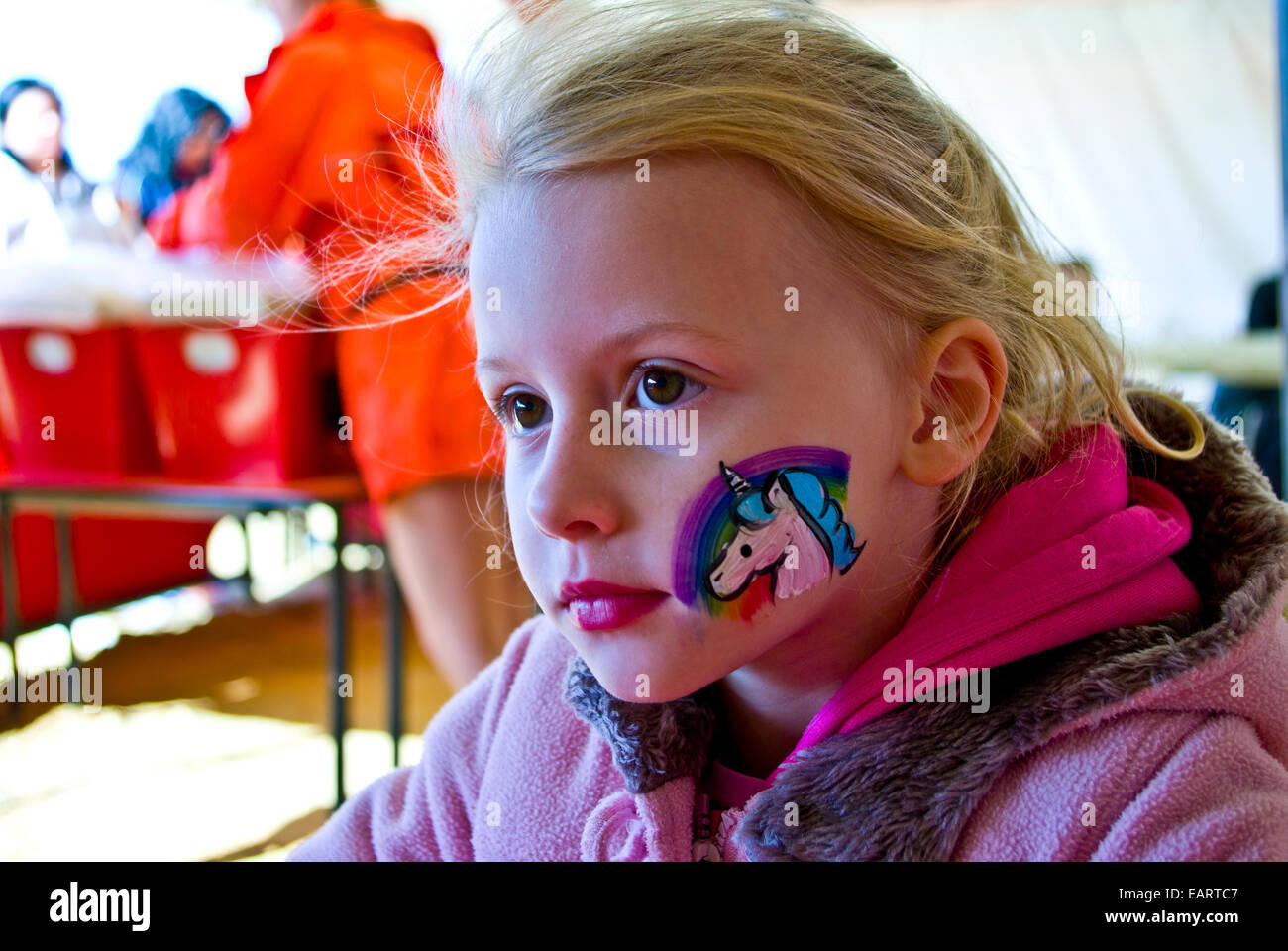 Une fille blonde avec une licorne arc-en-ciel et peint sur sa joue. Banque D'Images