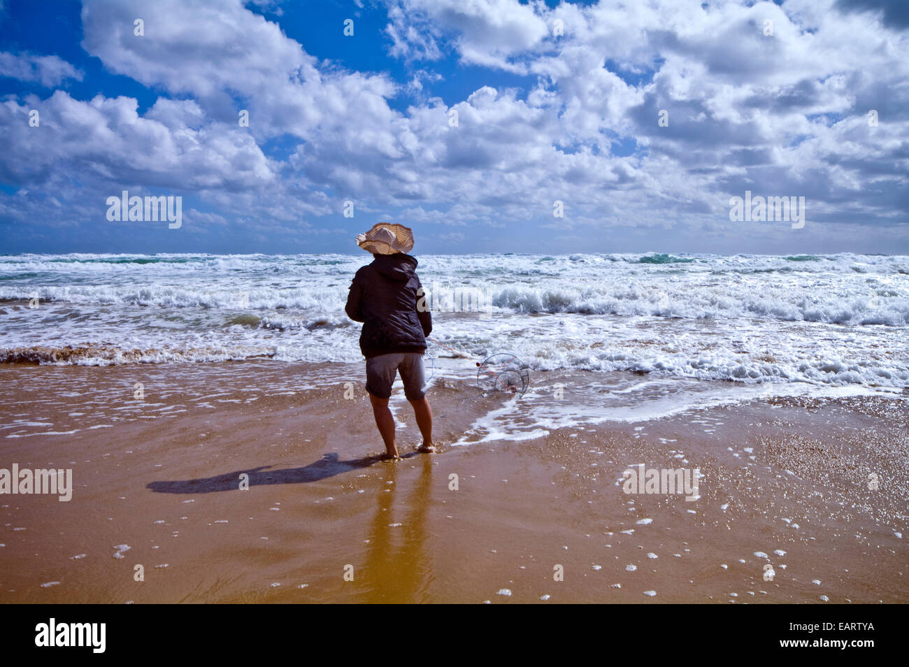 Une femme poissons pour pipi en utilisant une ligne de pêche et panier dans la surf. Banque D'Images