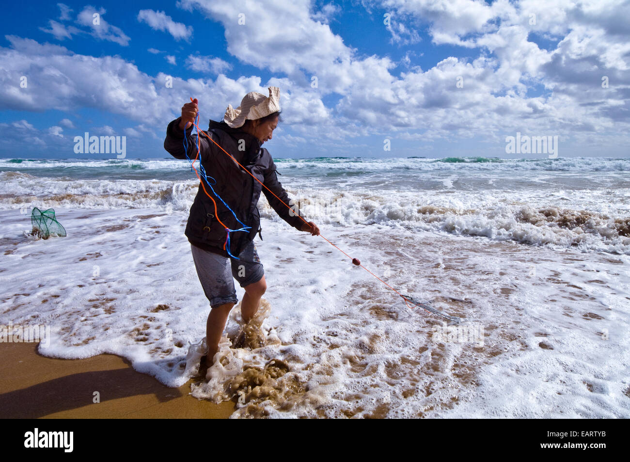 Une femme poissons pour pipi en utilisant une ligne de pêche et panier dans la surf. Banque D'Images
