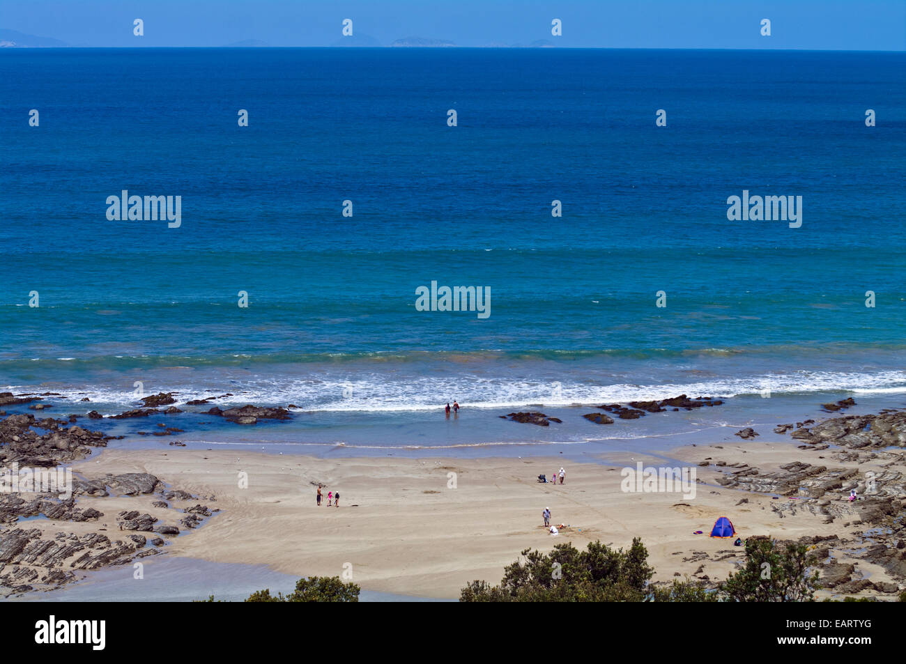 Les familles jouent sur une plage abritée par un océan turquoise. Banque D'Images