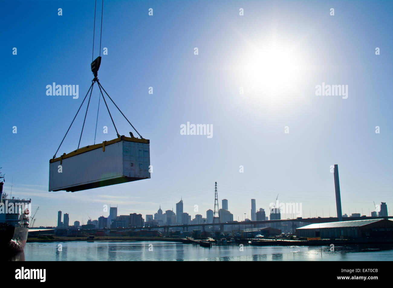 Une grue soulève un conteneur d'expédition sur une rivière au-delà d'un horizon de la ville. Banque D'Images