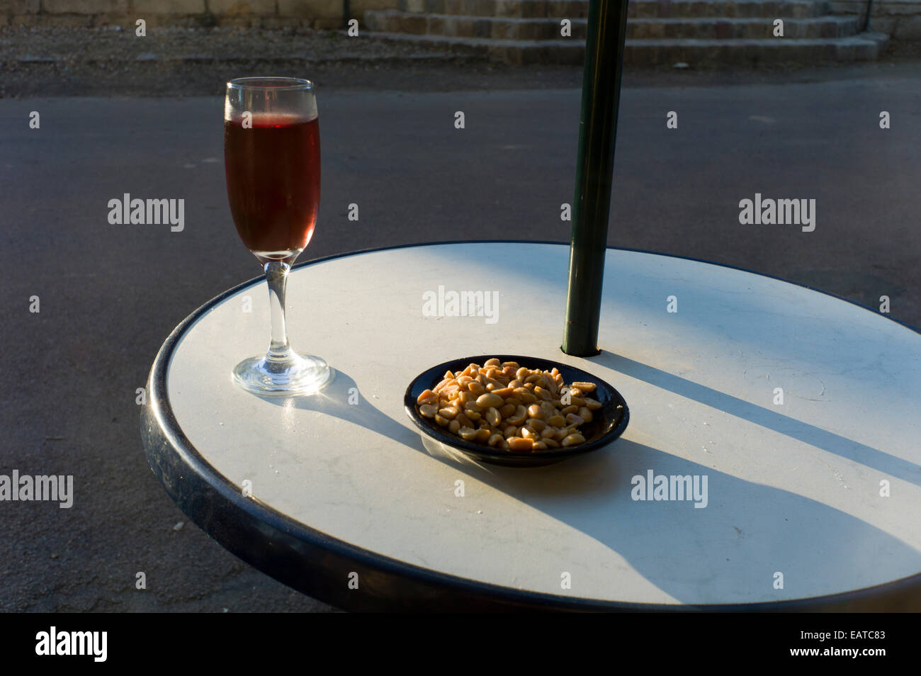 Verre de vin rose et arachides sur cafe table, soleil du soir Banque D'Images