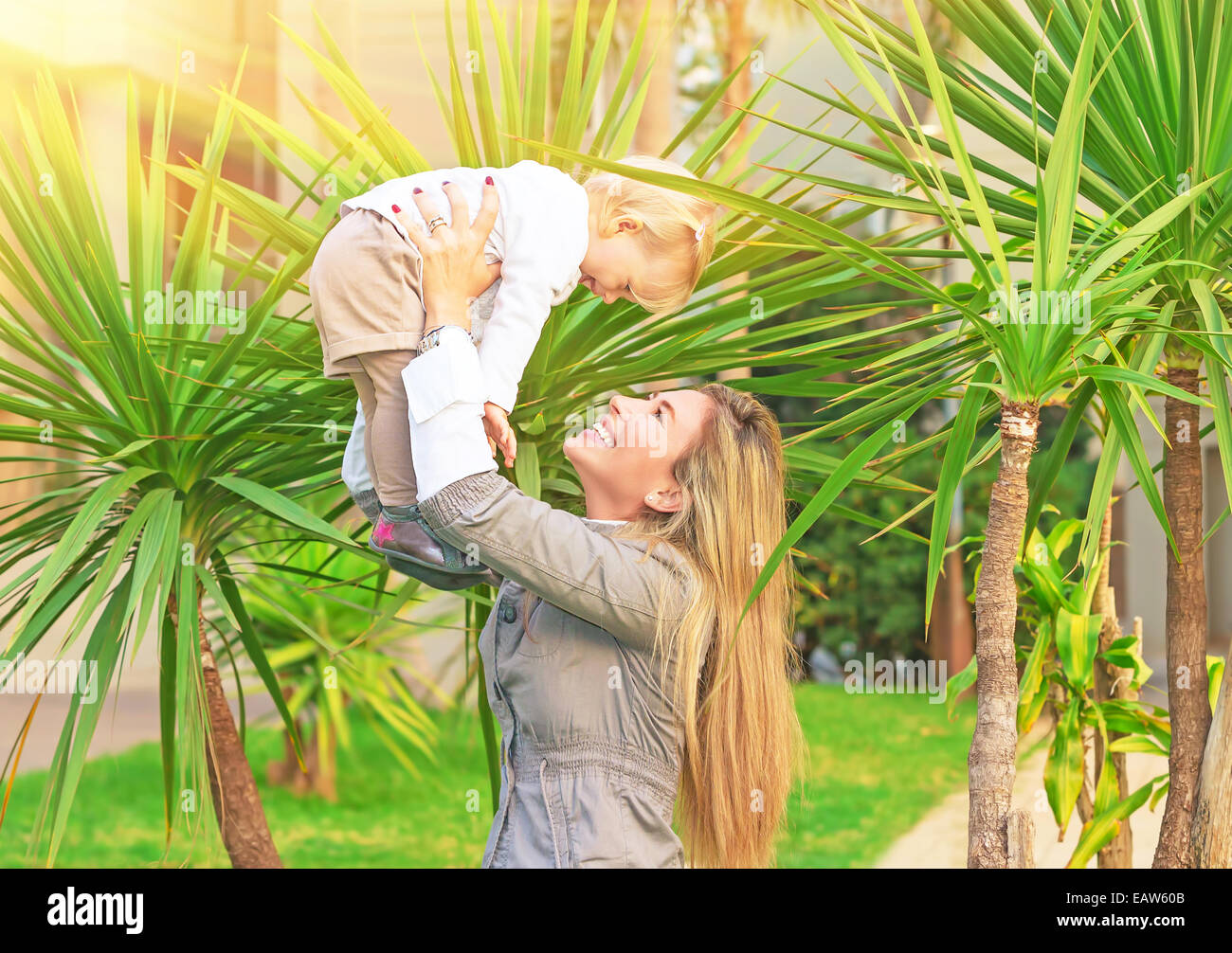 Cheerful woman with baby in fresh green palm parc, femme soulevant sa mignonne petite fille Banque D'Images