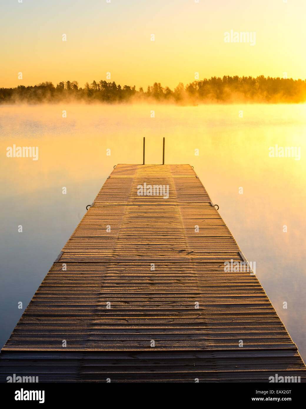 Dock en bois sur un lac brumeux au lever du soleil Banque D'Images