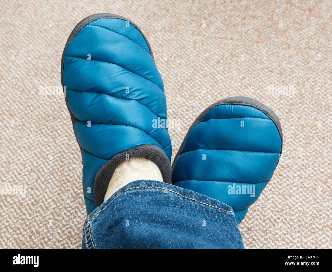 Une femme avec les pieds croisés portant une paire de jeans et des chaussons rembourrés sur le tapis à la maison vue d'en haut. En Angleterre, Royaume-Uni, Angleterre Banque D'Images