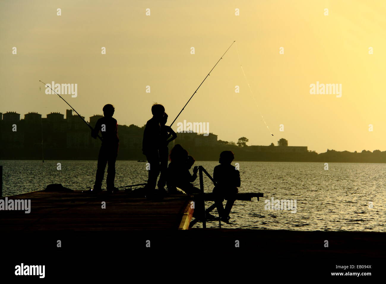 Silhouettes d'enfants s'amusant annonce la capture de poissons sur une jetée à soir d'été Banque D'Images