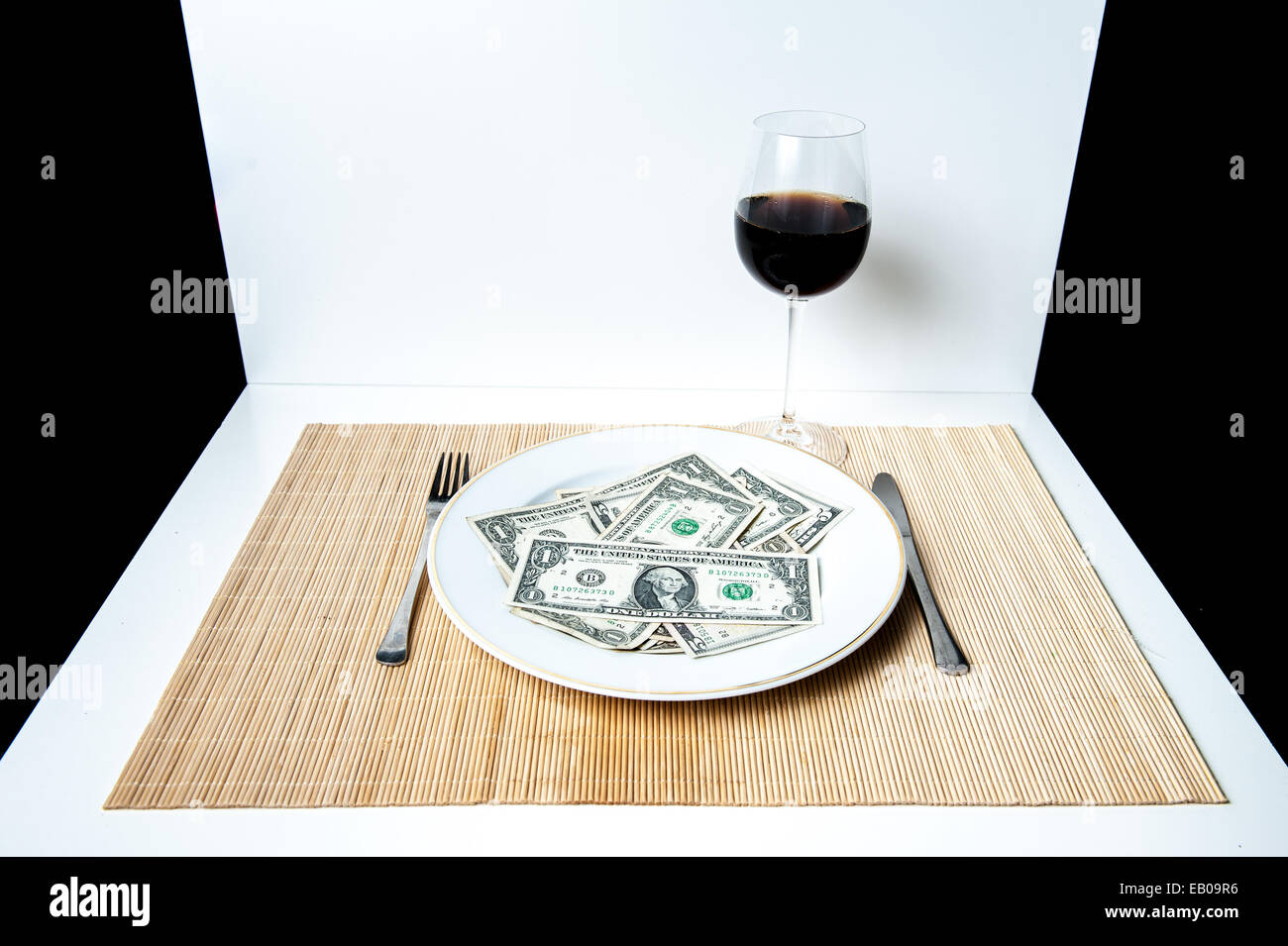 Une table avec du blanc et du noir en arrière-plan, une plaque avec beaucoup de dollars, fourchette, couteau et verre de vin Banque D'Images