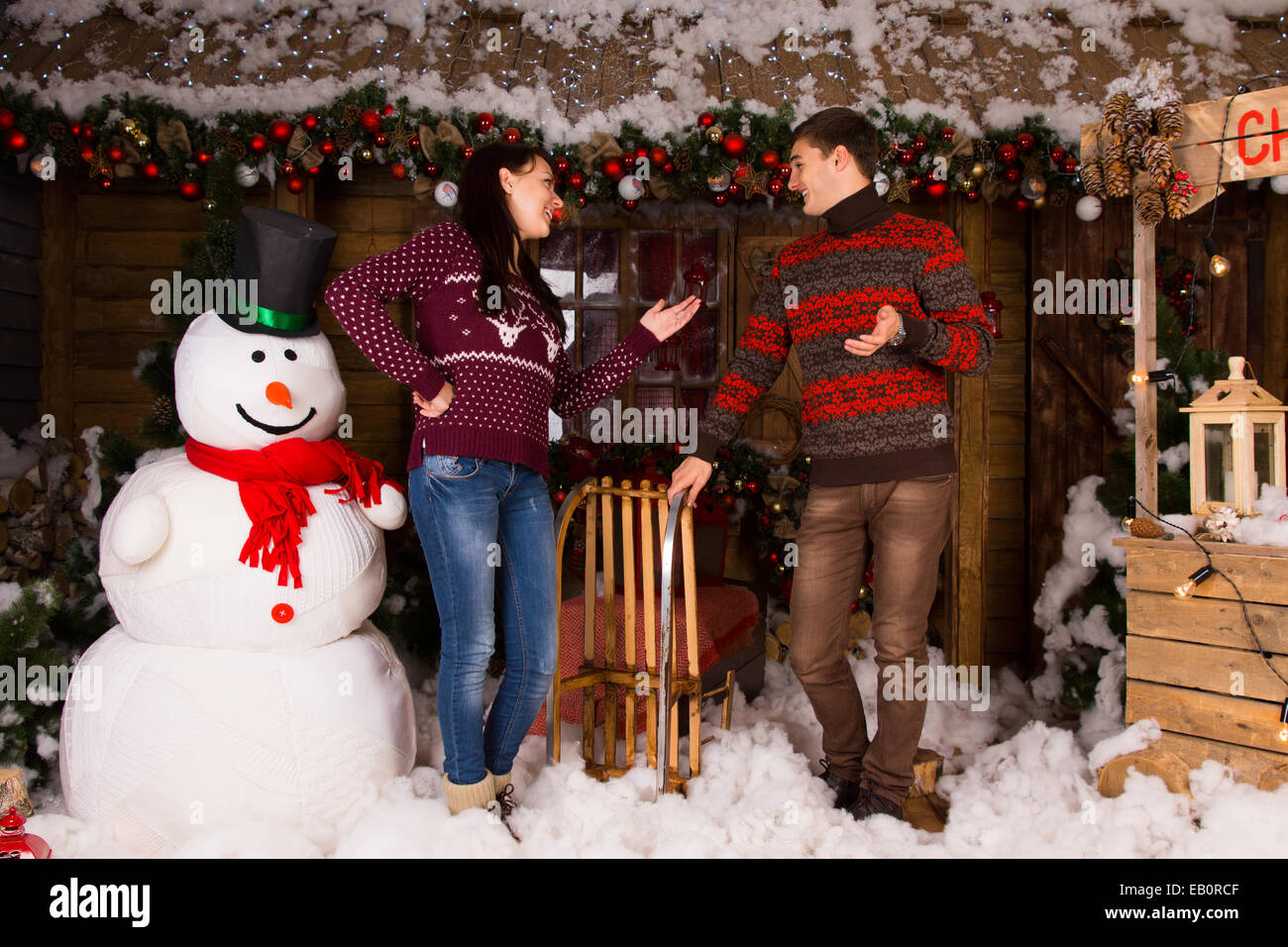 Jeune couple dans des tenues d'hiver à l'intérieur de parler la maison en bois, avec divers décors de Noël attrayant, grande piscine à côté de la neige Banque D'Images
