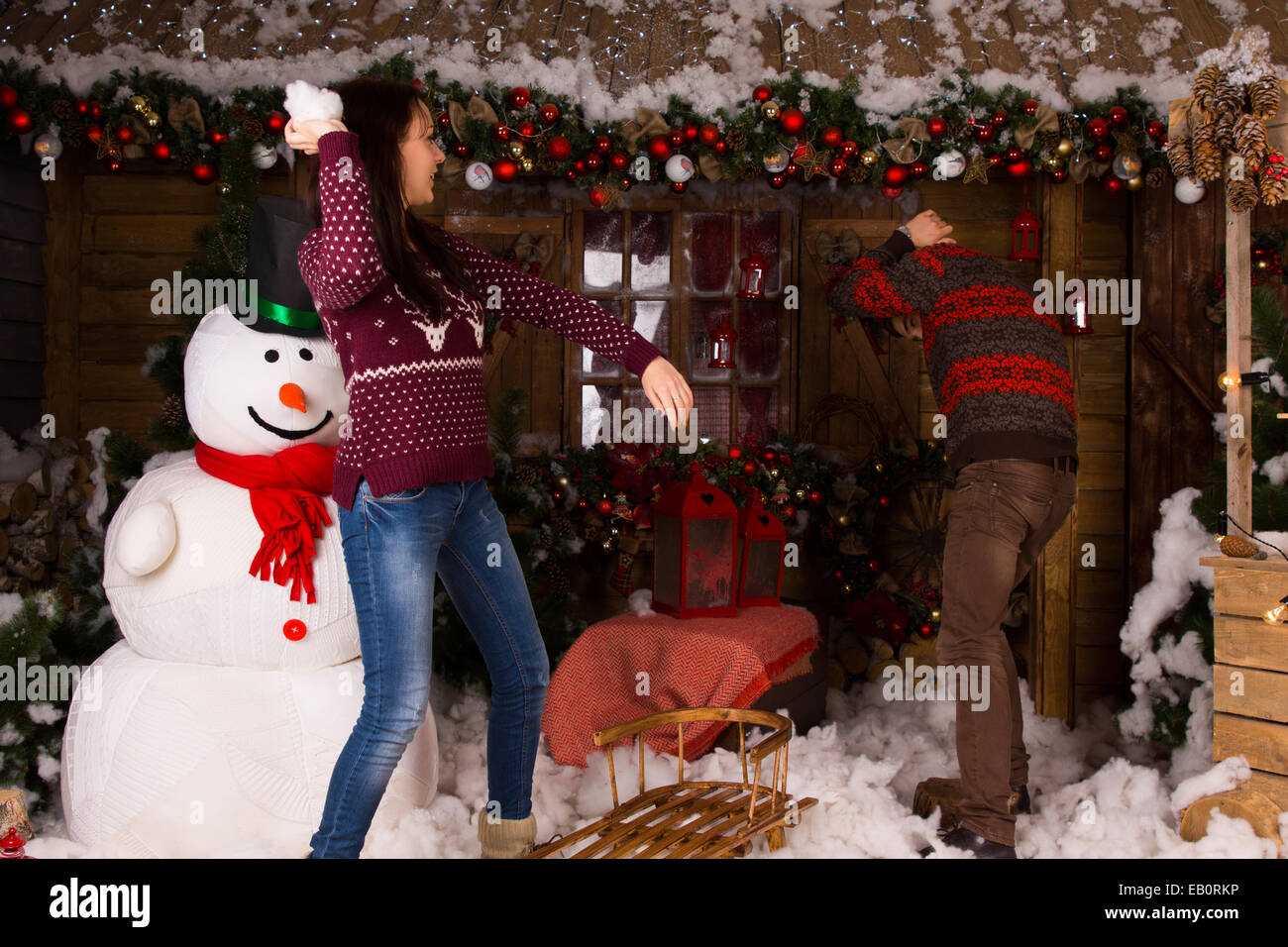 Jeune couple jouant avec du coton à l'intérieur de la neige Bonhomme et maison en bois avec différents décors de Noël. Banque D'Images