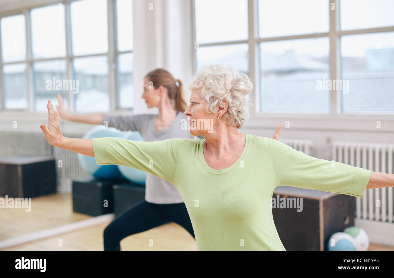 Deux femmes de faire des étirements et le yoga de l'exercice dans la salle de sport. Female trainer en arrière-plan avec des hauts femme en face pendant la formation. Banque D'Images