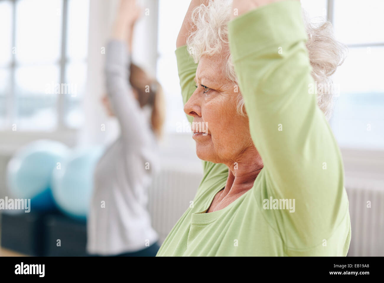 Close-up image of senior woman practicing yoga at gym. Active senior woman exercising at health club avec female trainer en retour Banque D'Images