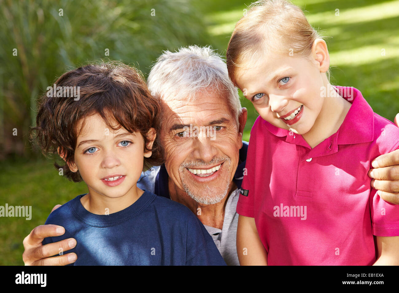 Grand-père de deux petits-enfants heureux dans un jardin verdoyant Banque D'Images