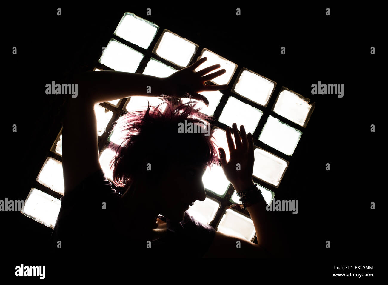 Une jeune adolescente femme prisonnière confinée dans une cellule de prison type location avec la lumière pénétrant par une fenêtre barrée Banque D'Images