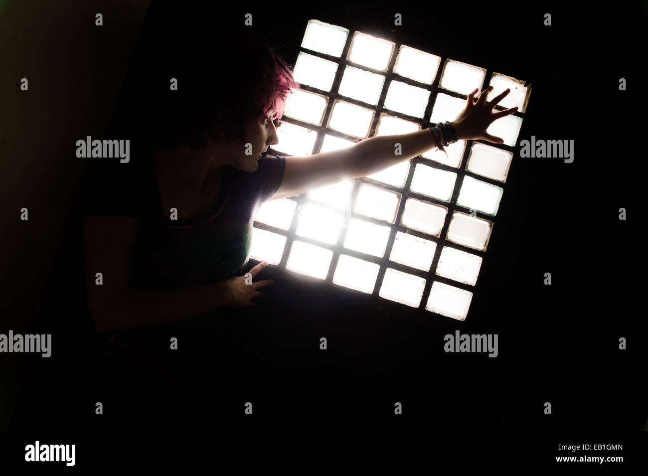 Une jeune adolescente femme prisonnière confinée dans une cellule de prison type location avec la lumière pénétrant par une fenêtre barrée Banque D'Images