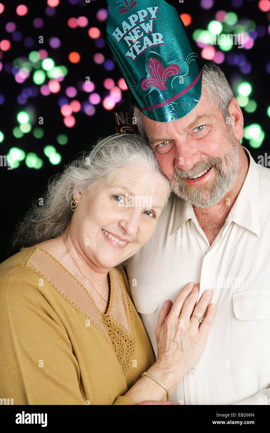 Beau couple dans la soixantaine qui pose pour un portrait romantique le soir du Nouvel An. D'artifice en arrière-plan. Banque D'Images