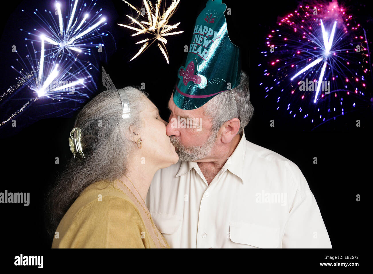 Beau couple à une fête du Nouvel An des baisers, sur le coup de minuit, comme l'artifice aller dans l'arrière-plan. Banque D'Images