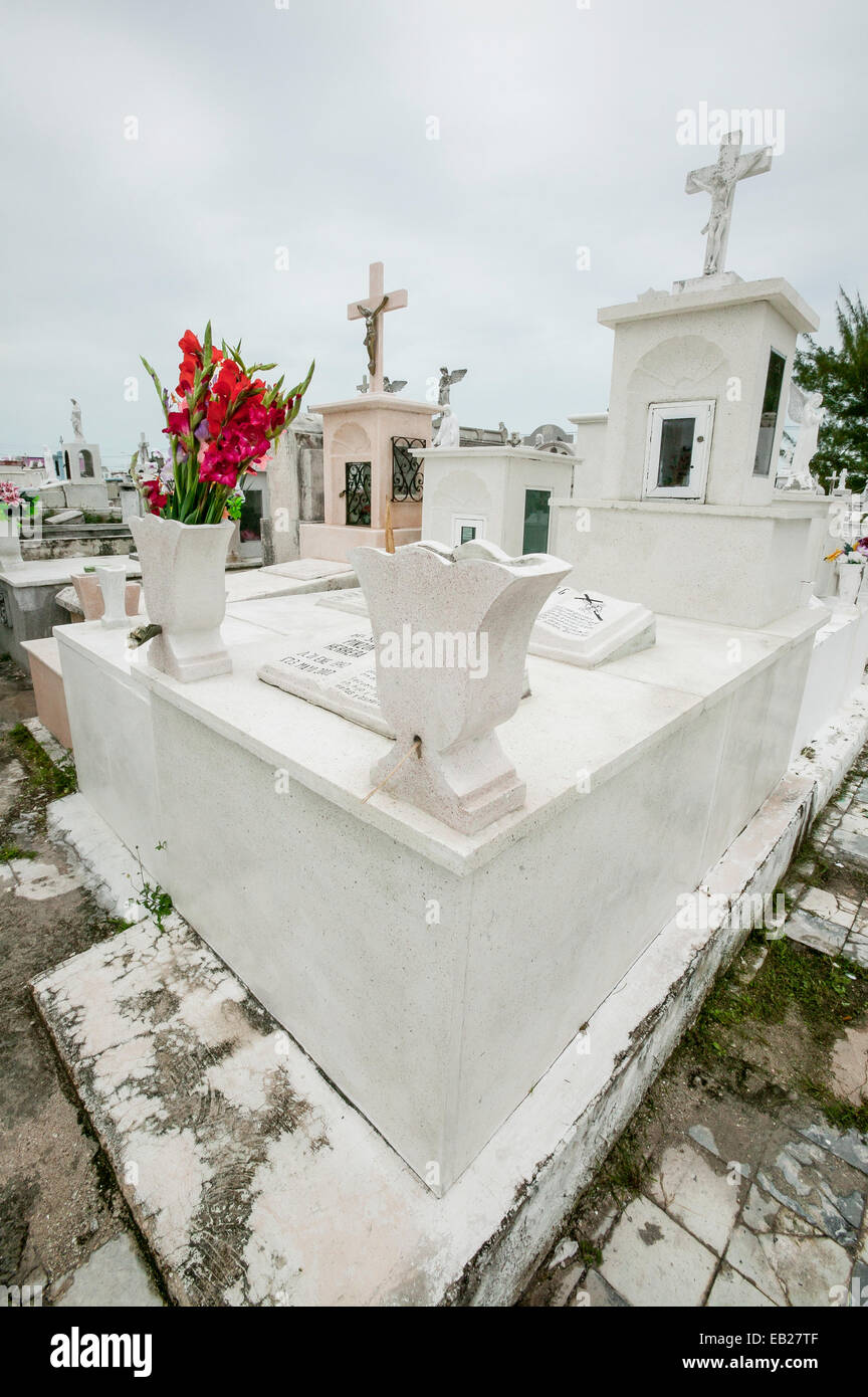 Blanc au-dessus de la terre tombe avec Jésus sur la croix, sculptures d'ange, et gladiolas rouges, cimetière Panteon de San Roman, Campeche, Mexique Banque D'Images