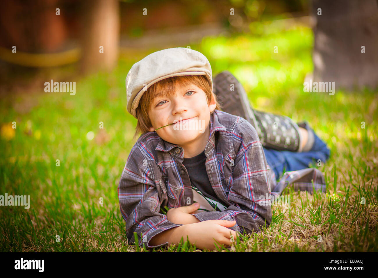 Boy lying on grass avec brin d'herbe dans la bouche Banque D'Images