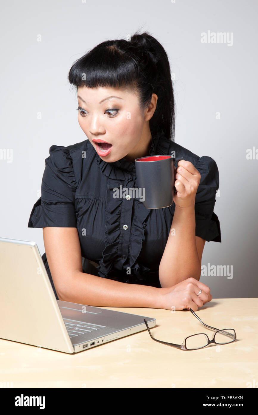 Surpris woman holding mug and looking at laptop Banque D'Images