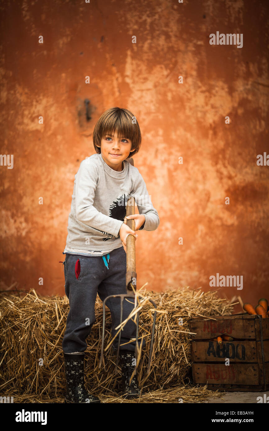 Garçon avec pitchfork debout par une balle de foin, Maroc Banque D'Images