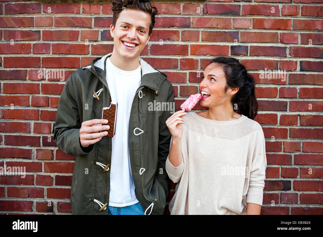 Caucasian couple eating ice cream près de red brick wall Banque D'Images