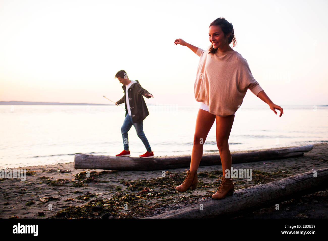 Caucasian couple walking on logs on beach Banque D'Images