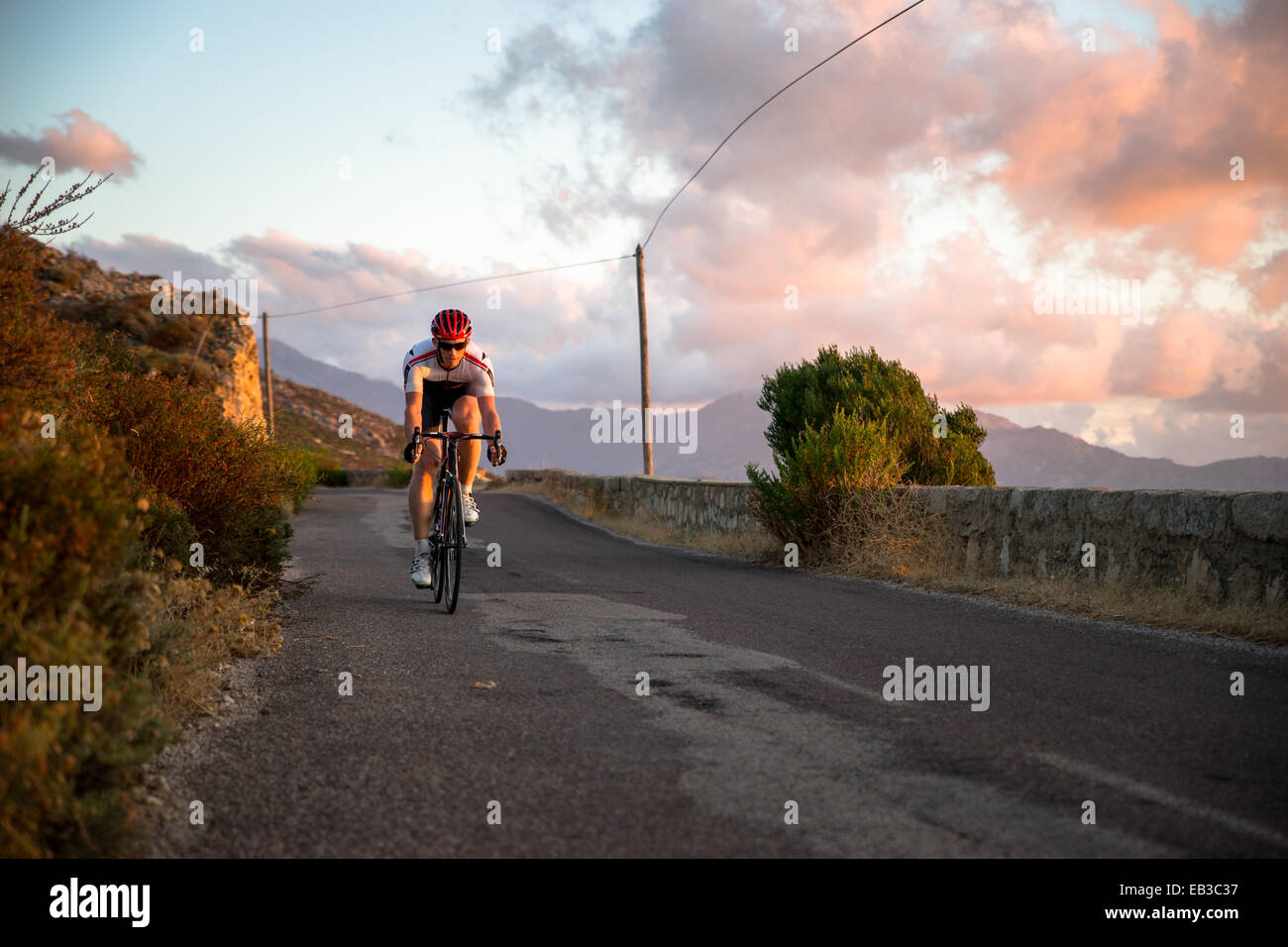 Homme en vélo le long d'une route côtière au coucher du soleil, Corse, France Banque D'Images