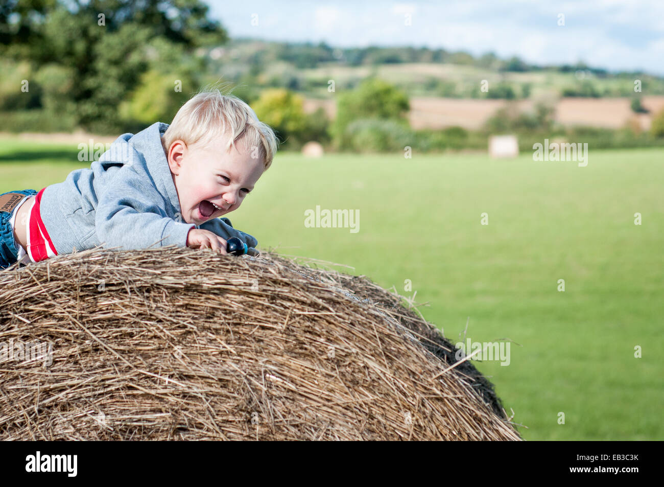 Boy crawling on hay bale laughing Banque D'Images
