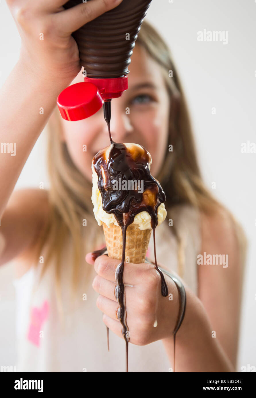 Messy Caucasian girl pouring sirop de chocolat sur ice cream cone Banque D'Images