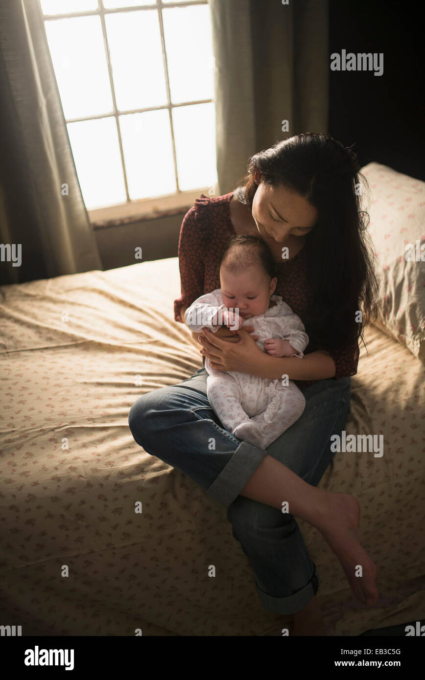 Asian mother holding baby on bed Banque D'Images