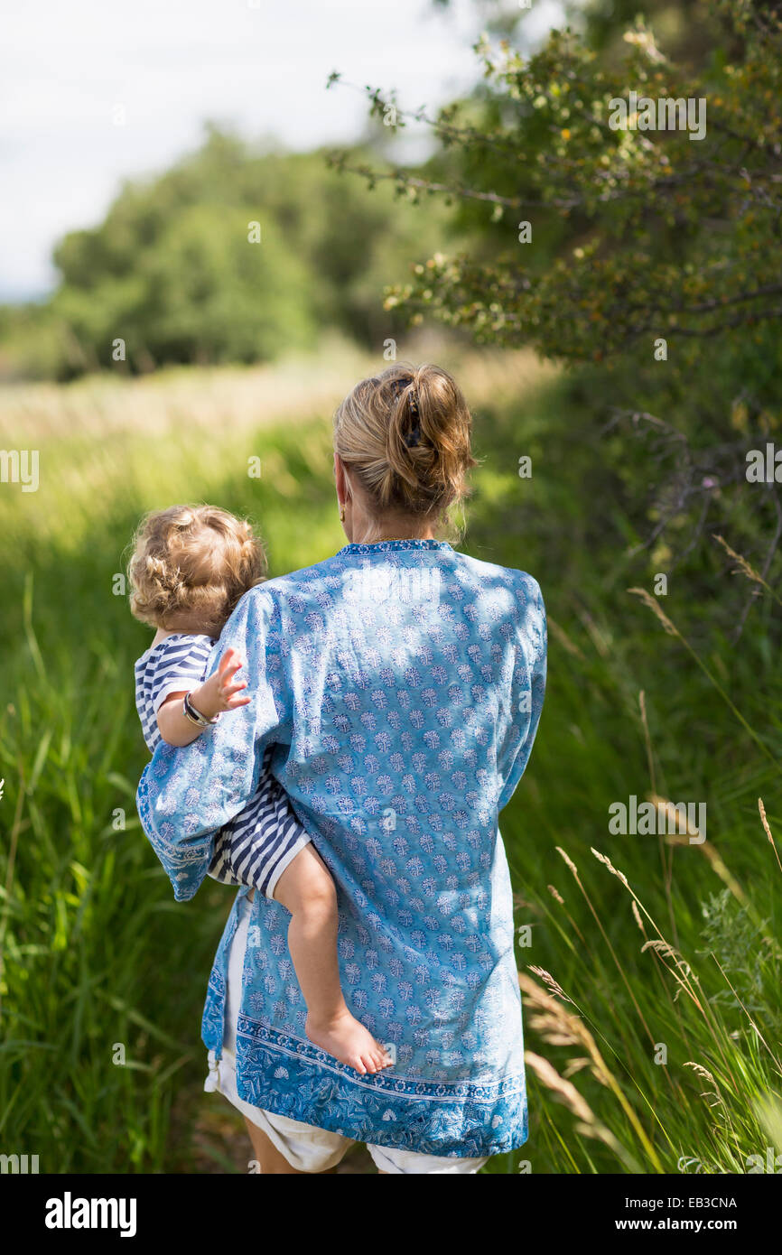 Caucasian mother carrying baby son in grassy field Banque D'Images