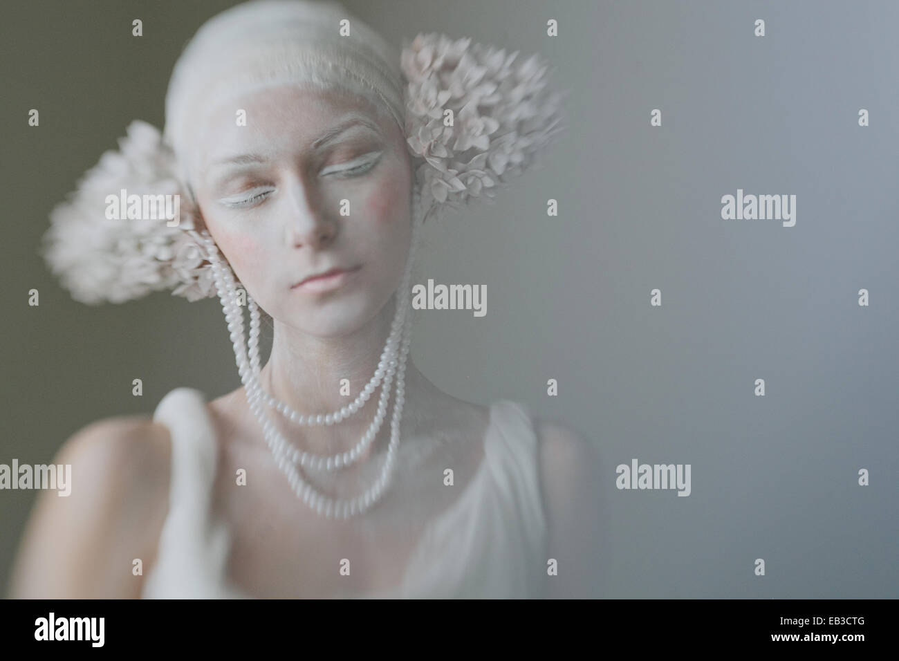 Portrait of young woman wearing composent, greasepaint, perles, et décorations de l'oreille de l'inflorescence ressemblant avec les yeux fermé Banque D'Images