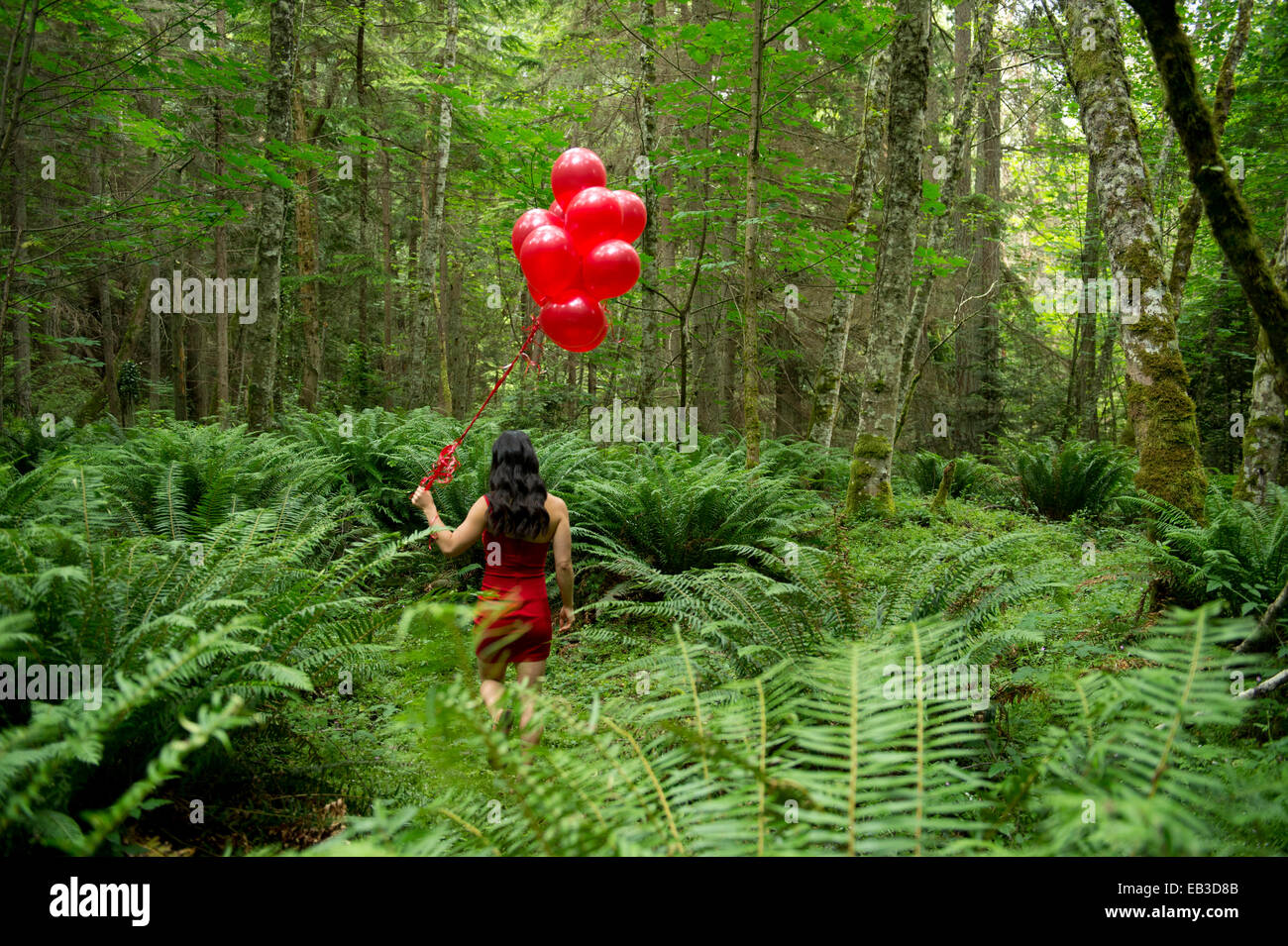 Korean woman holding red balloons dans une forêt luxuriante Banque D'Images