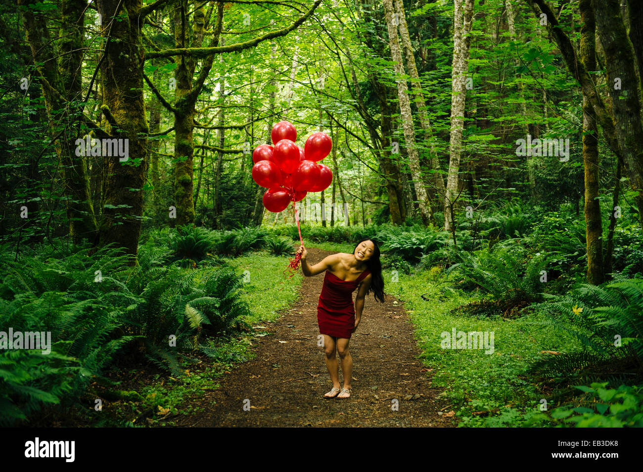 Korean woman holding red balloons dans une forêt luxuriante Banque D'Images