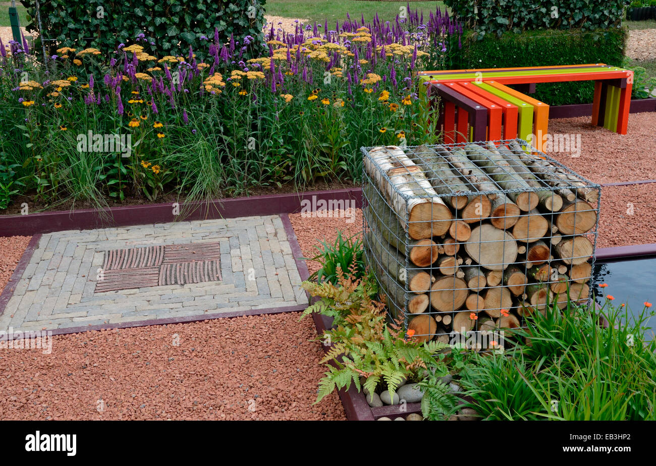 Une vue sur le jardin avec un banc et une cage de billes avec un insert décorative en pierre dans le jardin de fleurs avec chemin border Banque D'Images