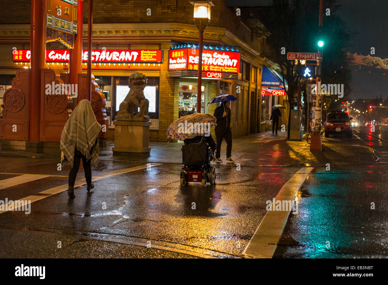 Homme handicapé en fauteuil roulant avec parapluie dans Chinatown sur rainy night-Victoria, Colombie-Britannique, Canada. Banque D'Images