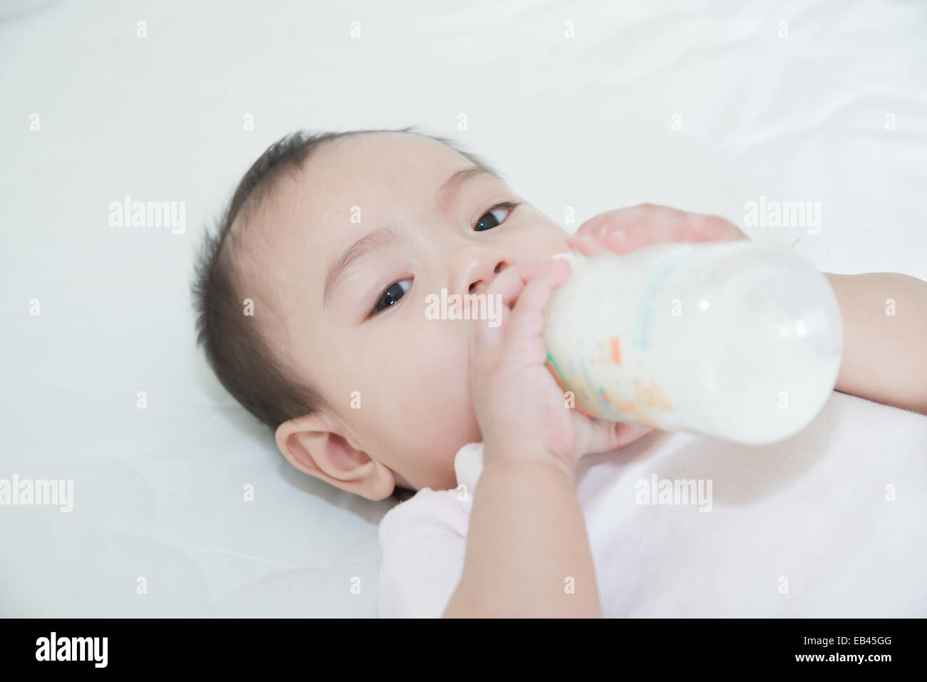 Jolie asiatique fille bébé boire du lait au lit Banque D'Images
