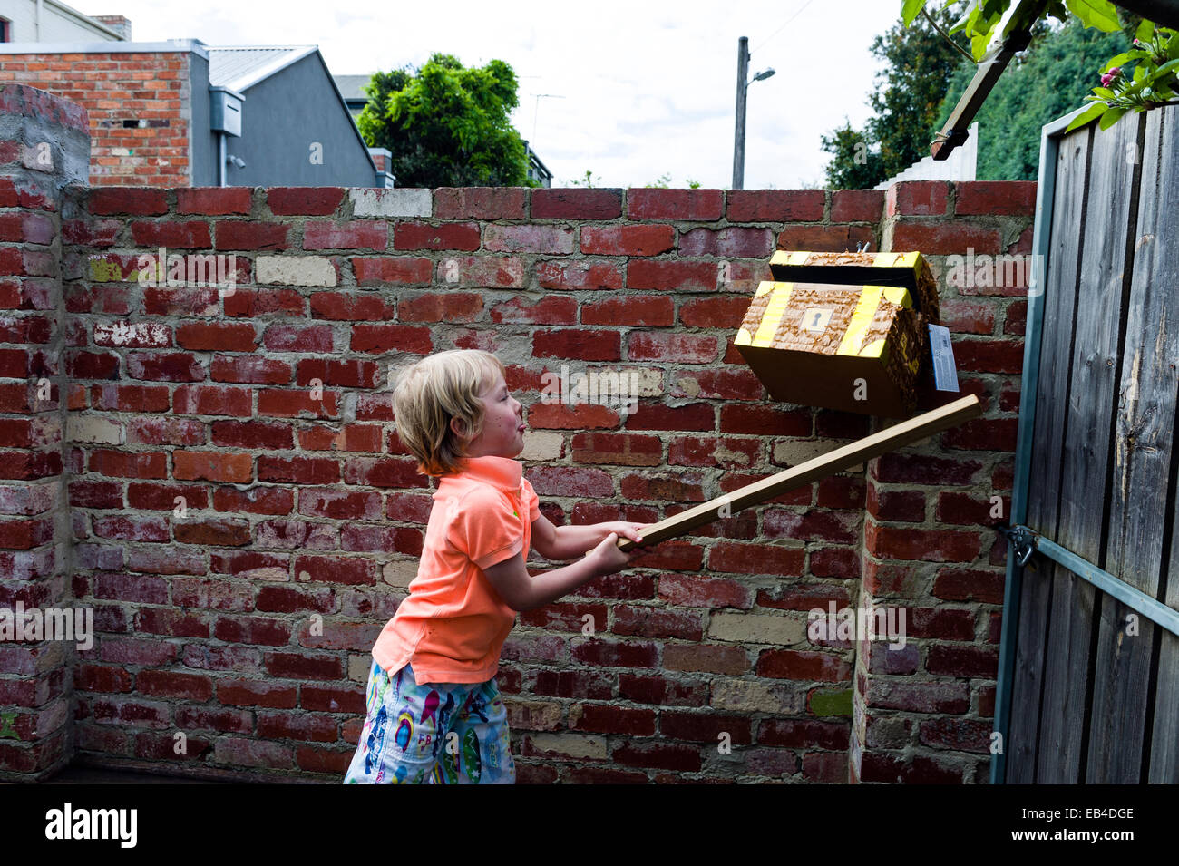 Un garçon à un anniversaire utilise un bâton pour essayer de casser une pinata en forme de coffre au trésor des pirates. Banque D'Images