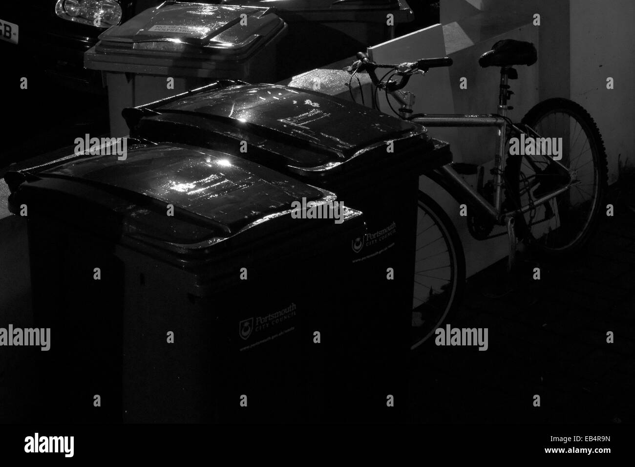 Location dans le jardin gauche à côté de poubelles éclairée par l'éclairage des rues la nuit sous une pluie battante Banque D'Images