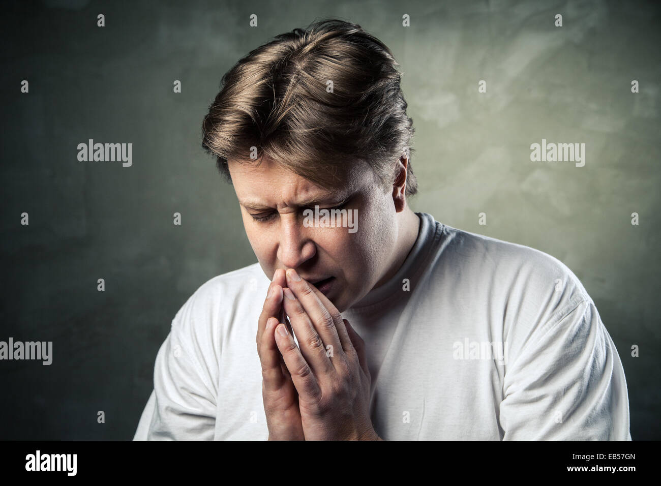 Jeune homme priant sur fond sombre studio Banque D'Images
