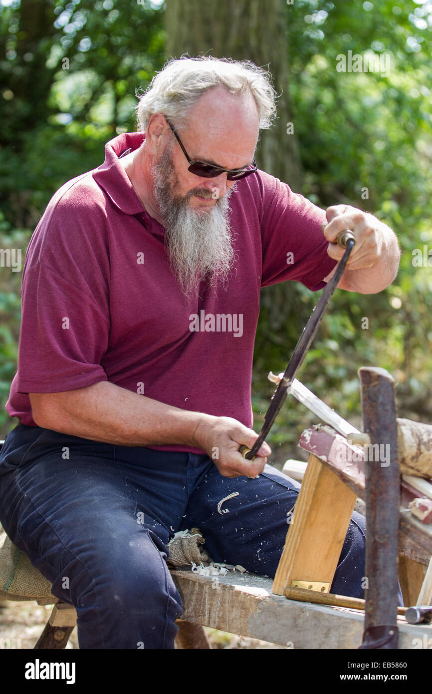 Un tanneur ou 'bodger' utilise une plane pour préparer un travail pour plus de douves de bois dans une clairière ensoleillée woodland Banque D'Images