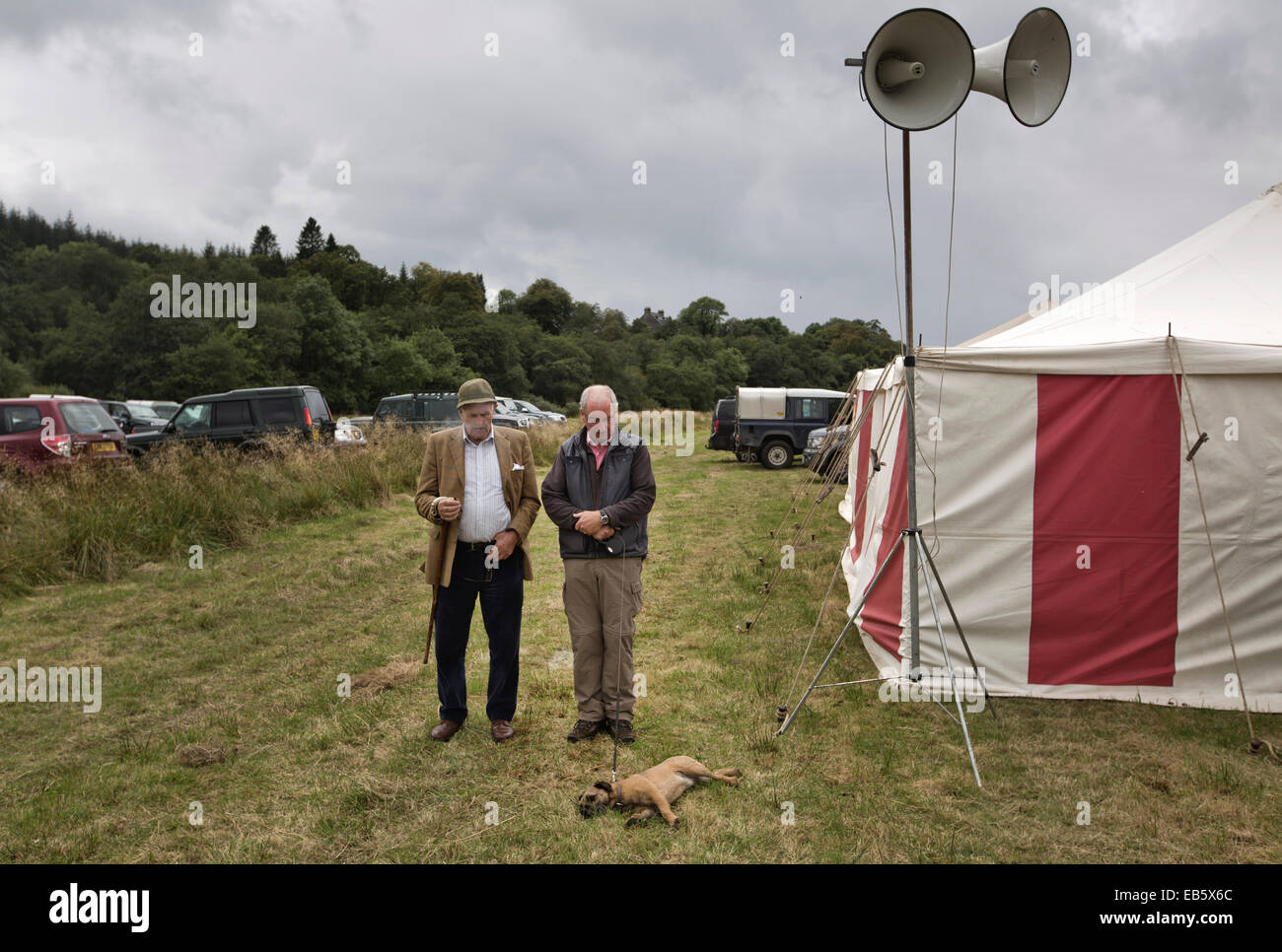 Deux hommes et un chien terrier debout à côté d'un chapiteau regardant le Dalmally Agricultural Society Show à Dalmally, en Écosse. Banque D'Images