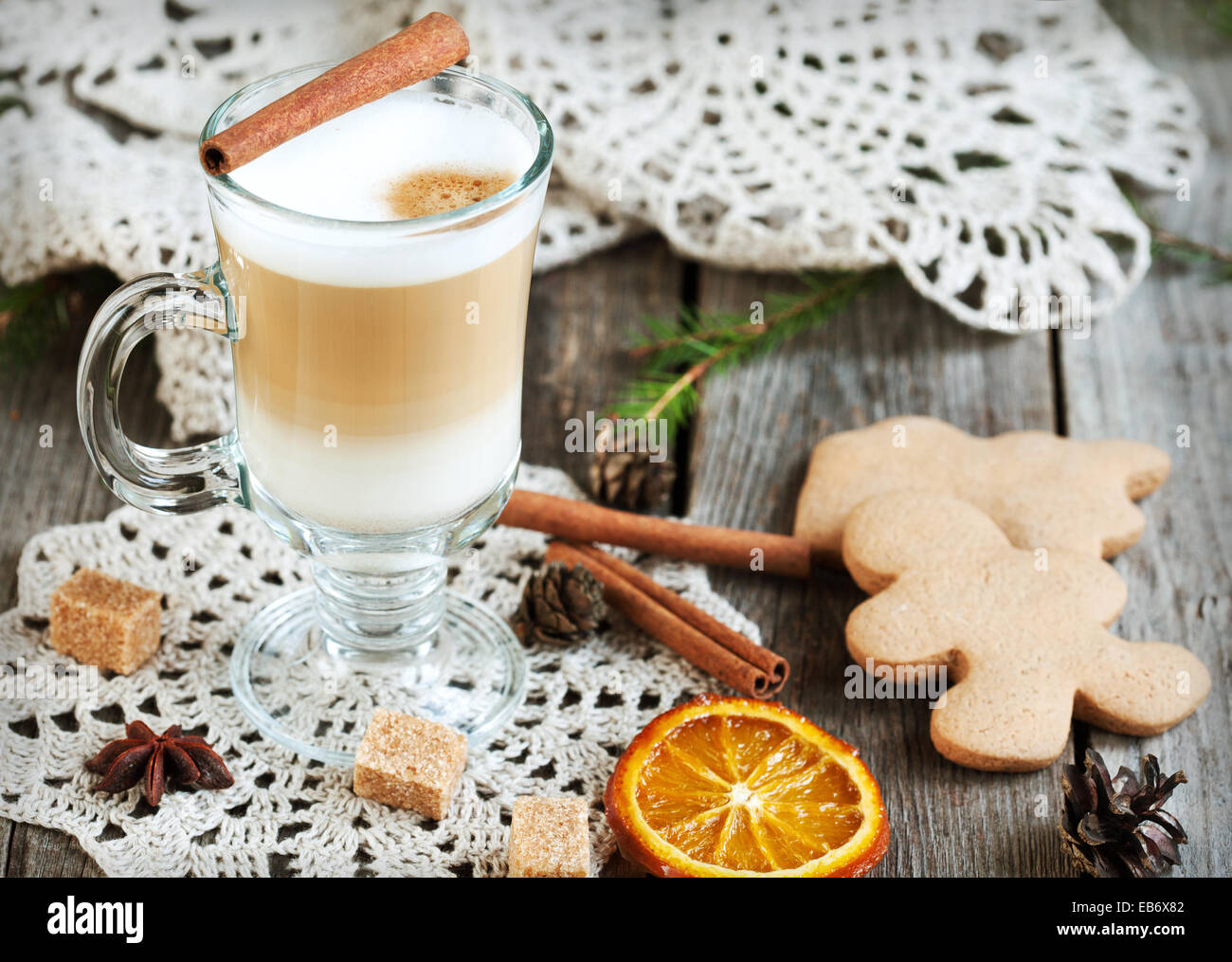Café chaud avec du lait dans un verre sur une table en bois avec des morceaux de sucre, des bâtons de cannelle et d'orange confites tranche Banque D'Images
