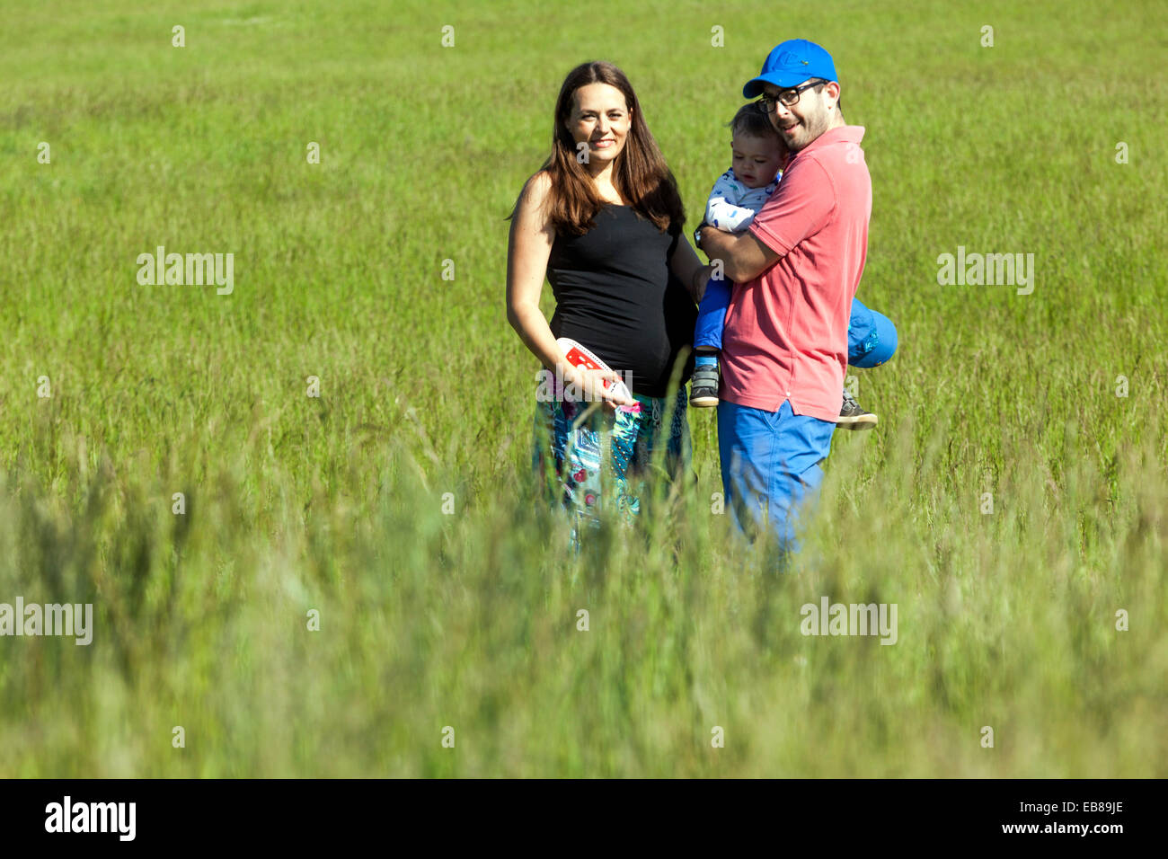 Une famille heureuse, une femme enceinte avec son mari et petit garçon passer du temps ensemble et de jouer à des jeux dans une prairie d'été Banque D'Images