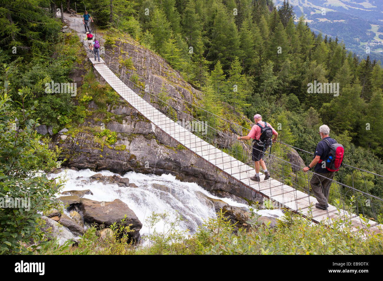 Les randonneurs sur le Tour du Mont Blanc traverser un pont suspendu sur la rivière de fonte du glacier de Bionnassay. Banque D'Images