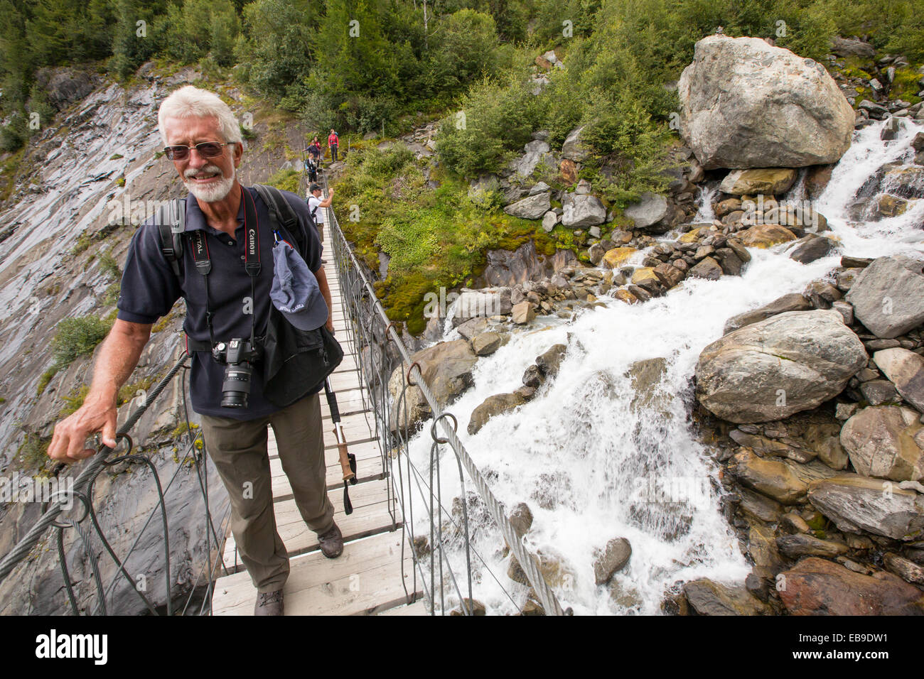 Les randonneurs sur le Tour du Mont Blanc traverser un pont suspendu sur la rivière de fonte du glacier de Bionnassay. Banque D'Images
